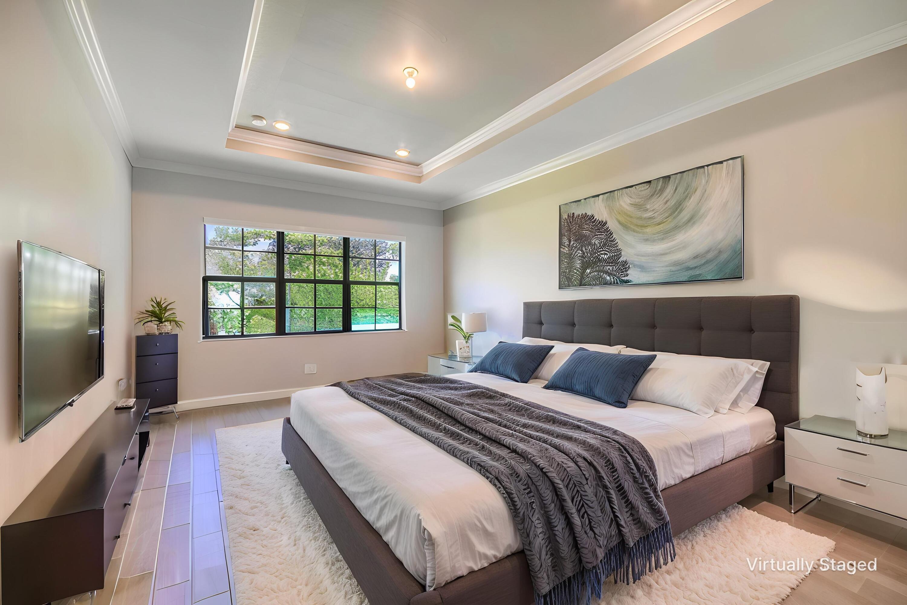 Bedroom with a large bed, dark upholstered headboard, tray ceiling, and grid-framed window.