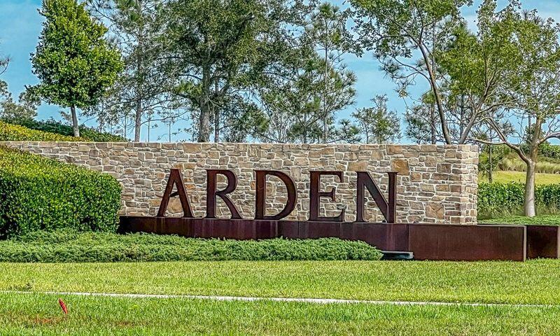 Arden entrance sign on a stone wall, framed by hedges and a broad green lawn.