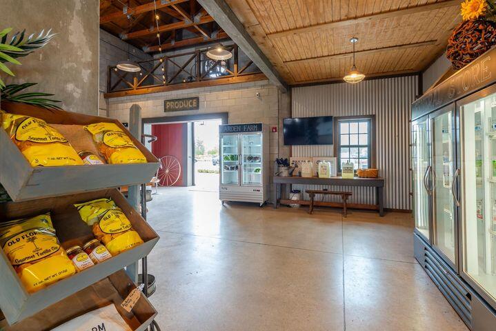 Farm-market interior with stocked produce shelves, glass-front refrigerators, and a high wood-plank ceiling.