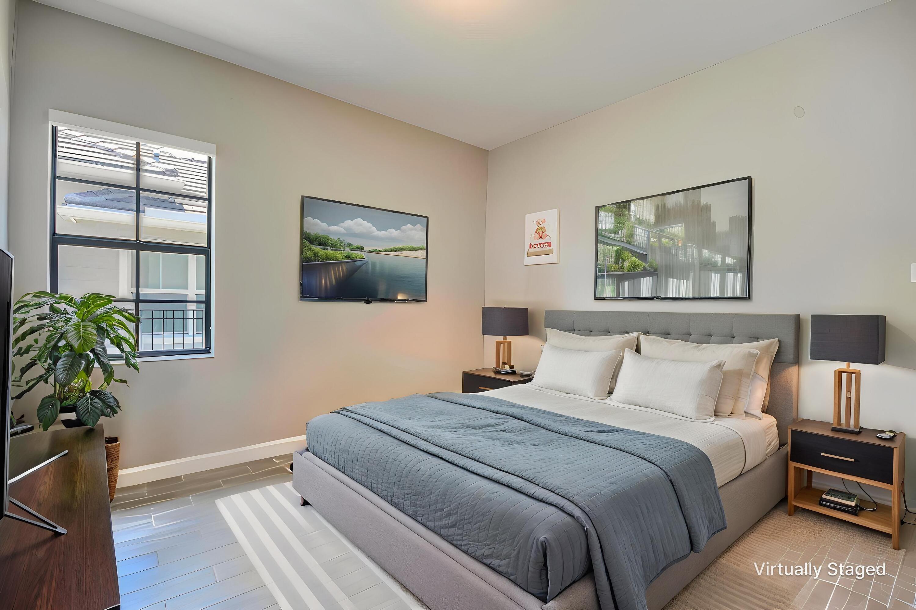 Bedroom with a white bed, blue-gray quilt, matching nightstands, framed art, and a window with blinds.