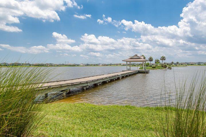 Lakeside dock stretches from a grassy shore to a covered pavilion, with reeds in the foreground.