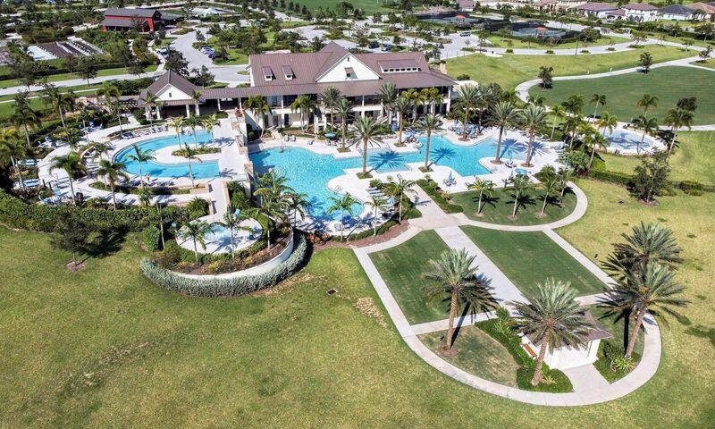 Aerial view of a clubhouse and bright-blue pools surrounded by palm trees and curving paths.