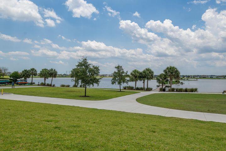 Lakeside lawn with a curving path, shoreline trees, and a partly cloudy sky.
