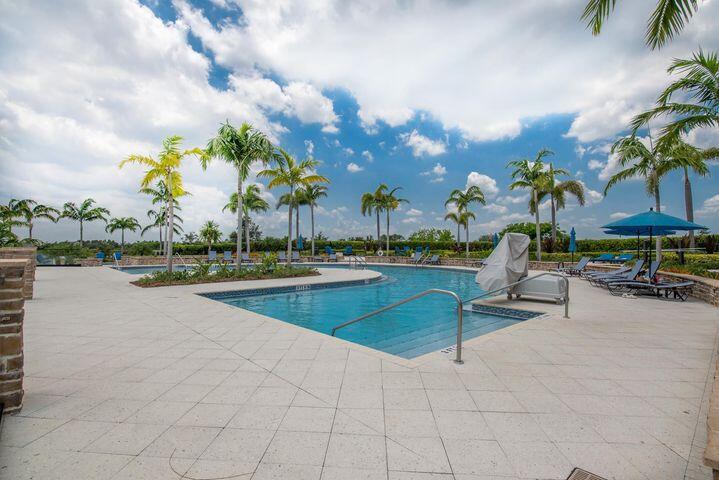 Outdoor pool with palm trees, lounge chairs, and a blue umbrella on a tiled deck.