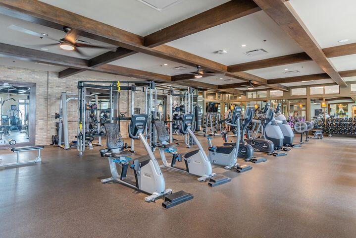 Fitness center with rows of exercise machines beneath exposed wooden ceiling beams.