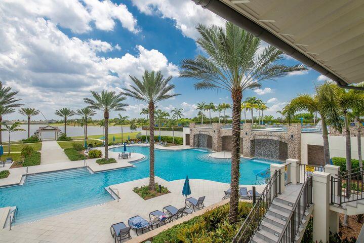 Community pool with curved blue water, palm trees, lounge chairs, and steps beside the deck.