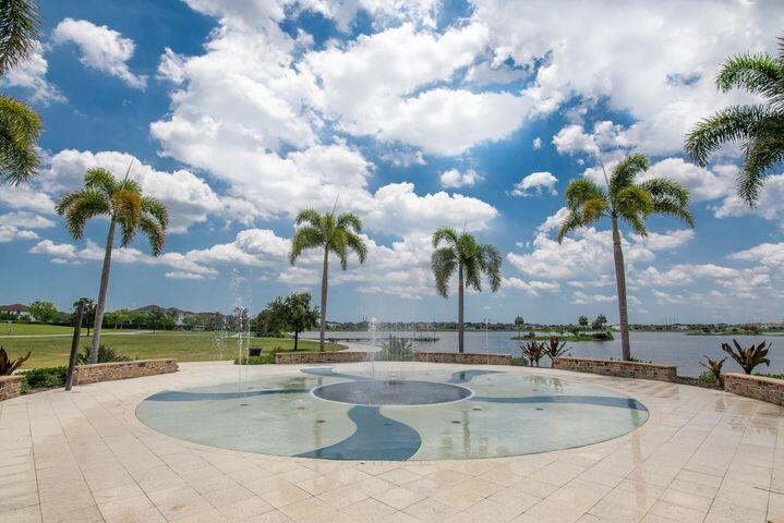 Curved pool and pale stone patio overlook a lake lined with palm trees.