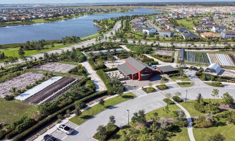 Aerial property with a red-roofed building, agricultural plots, nearby lake, and residential neighborhood.