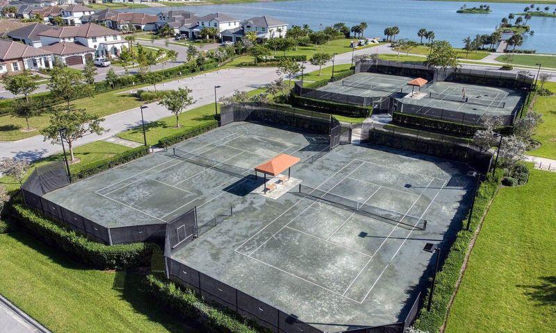 Fenced tennis courts with orange shade canopies, surrounded by lawns and homes.