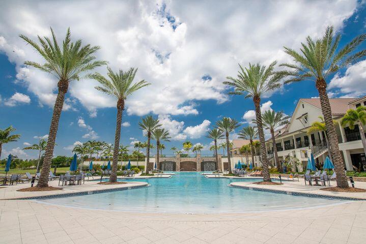 Community pool lined with palm trees, lounge chairs, blue umbrellas, and a clubhouse.