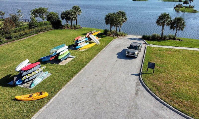 Waterfront lawn with palm trees, kayaks and paddleboards beside a paved driveway.