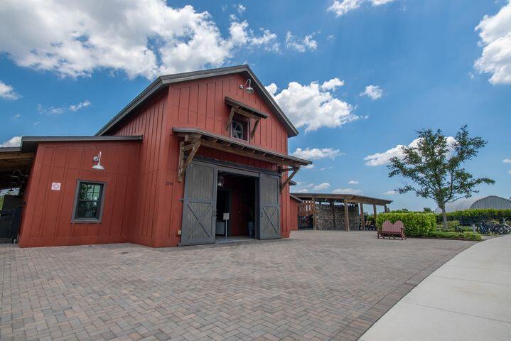 Red barn-style building with open double doors beside a broad paved courtyard.