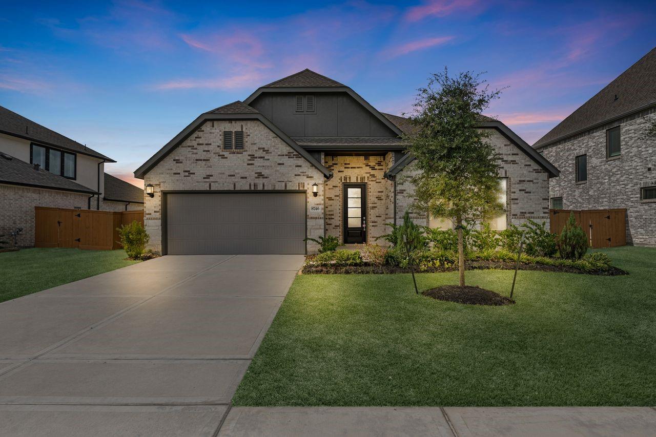 Brick-and-siding home with a two-car garage, landscaped lawn, and driveway at dusk.
