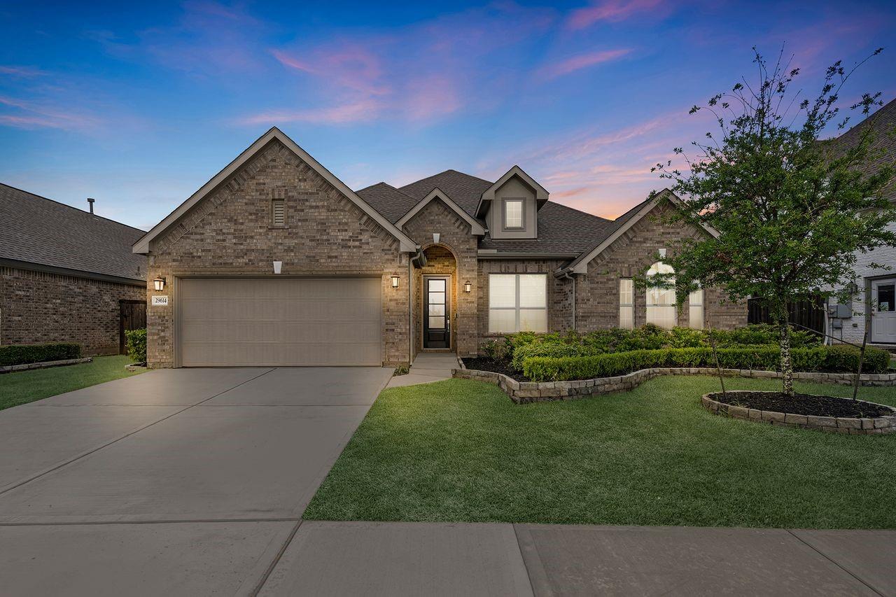 Brick house with a two-car garage and landscaped front yard beneath a colorful dusk sky.