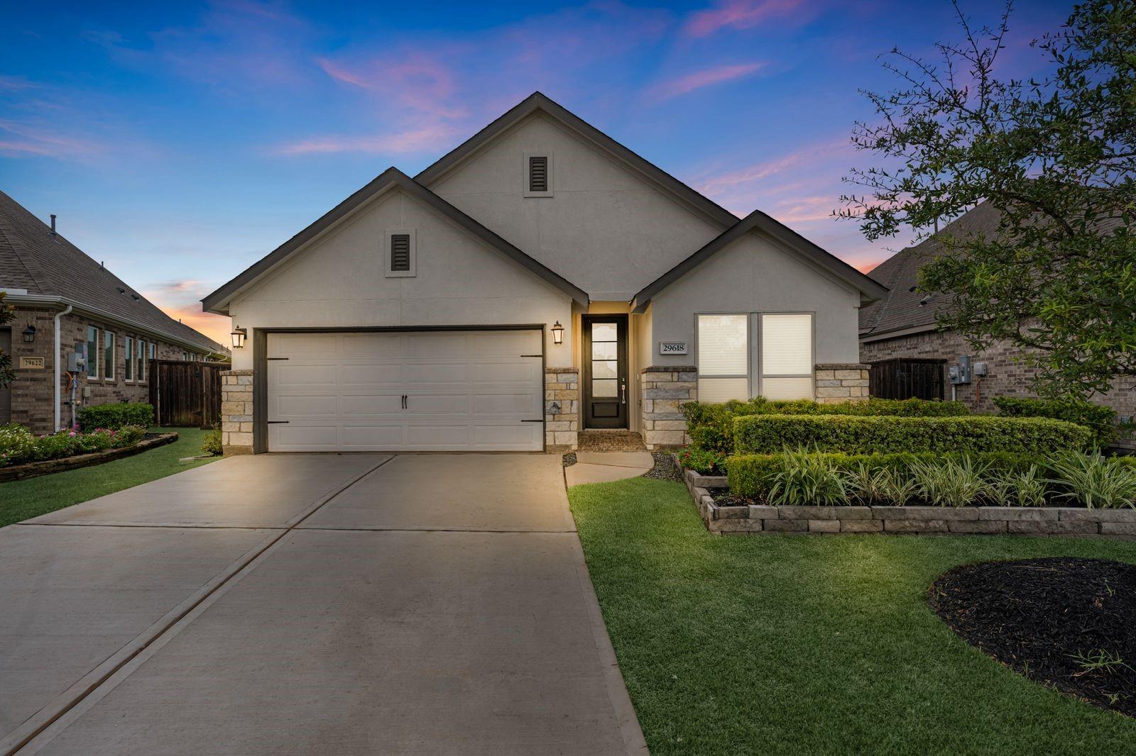 Single-story home with a two-car garage, stone accents, and landscaped yard at dusk.