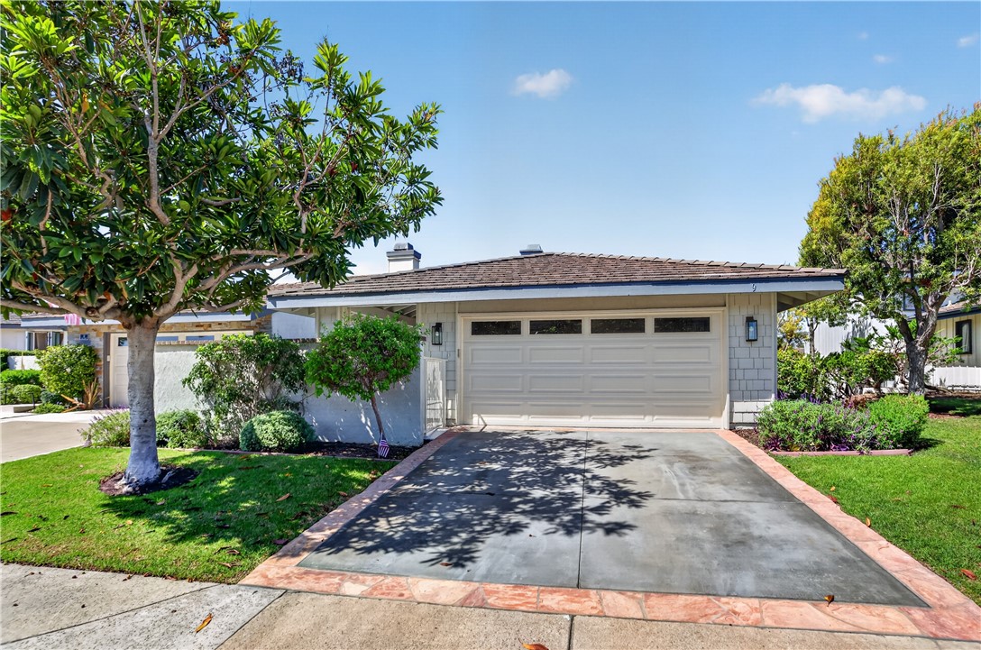 Single-story home with a wide garage and driveway, framed by mature trees and landscaped front yard.