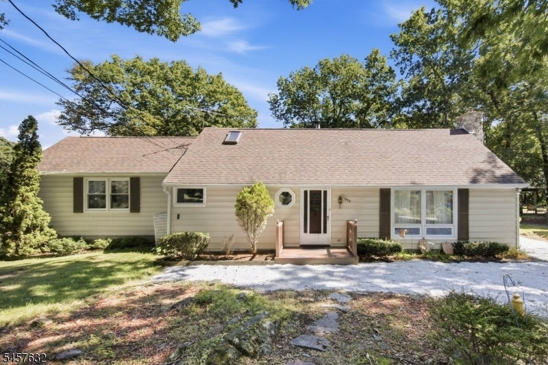 Single-story beige house with a small covered entry and gravel driveway beneath mature trees.