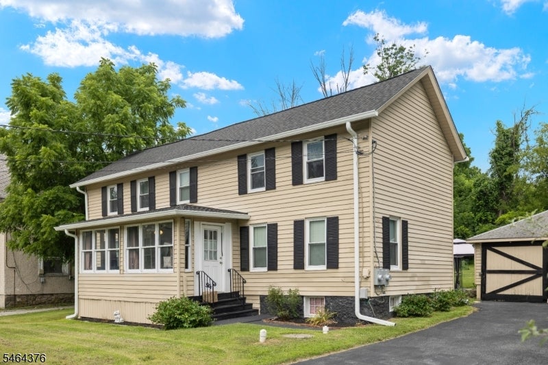 Beige two-story house with an enclosed front porch, black shutters, and a detached garage.