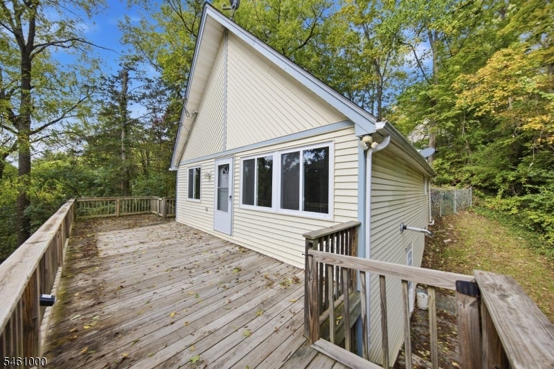 Light-colored gable-roofed house with a broad wooden deck surrounded by trees.