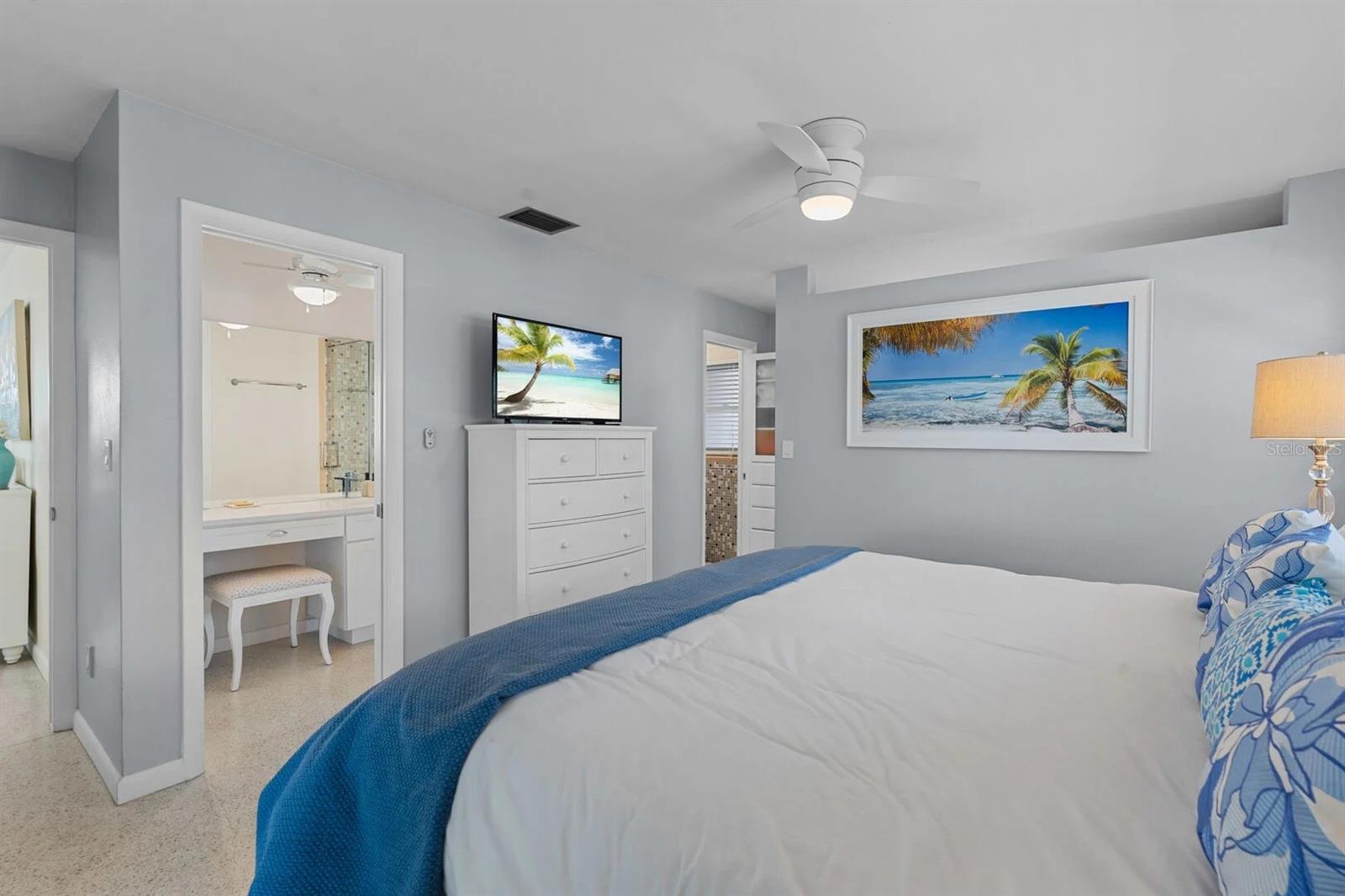 Bedroom with a white bed, blue throw, ceiling fan, and open vanity area.