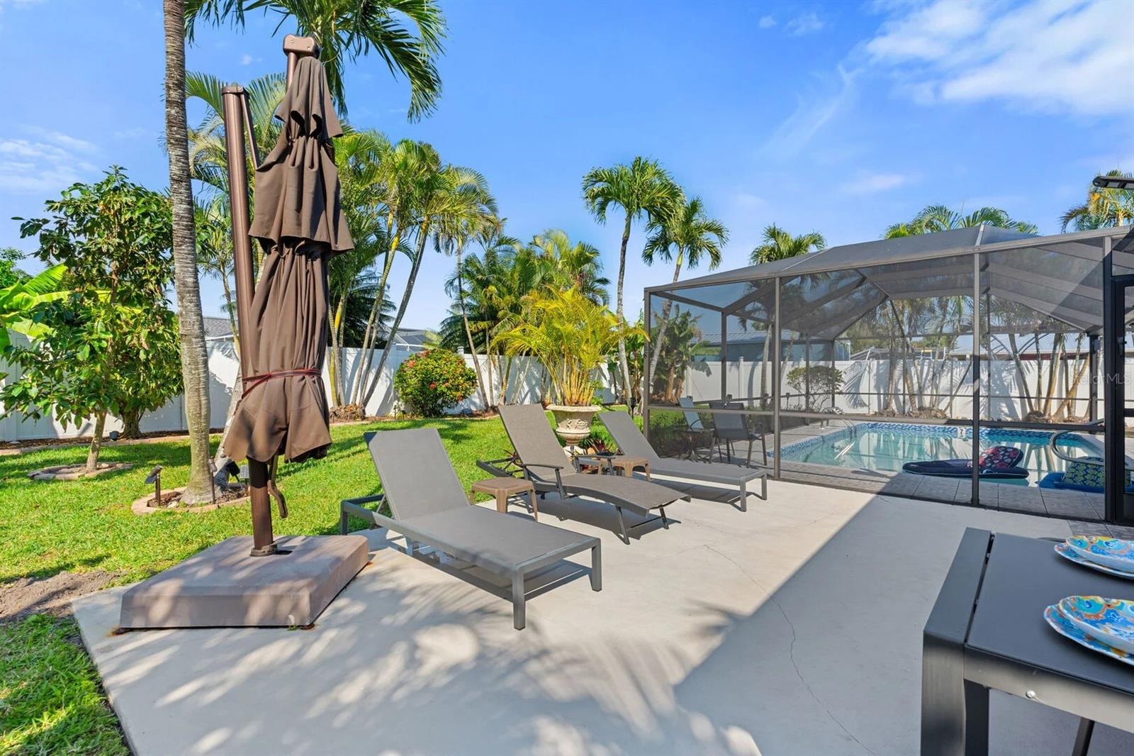Backyard pool and patio with screened enclosure, lounge chairs, and palm trees.