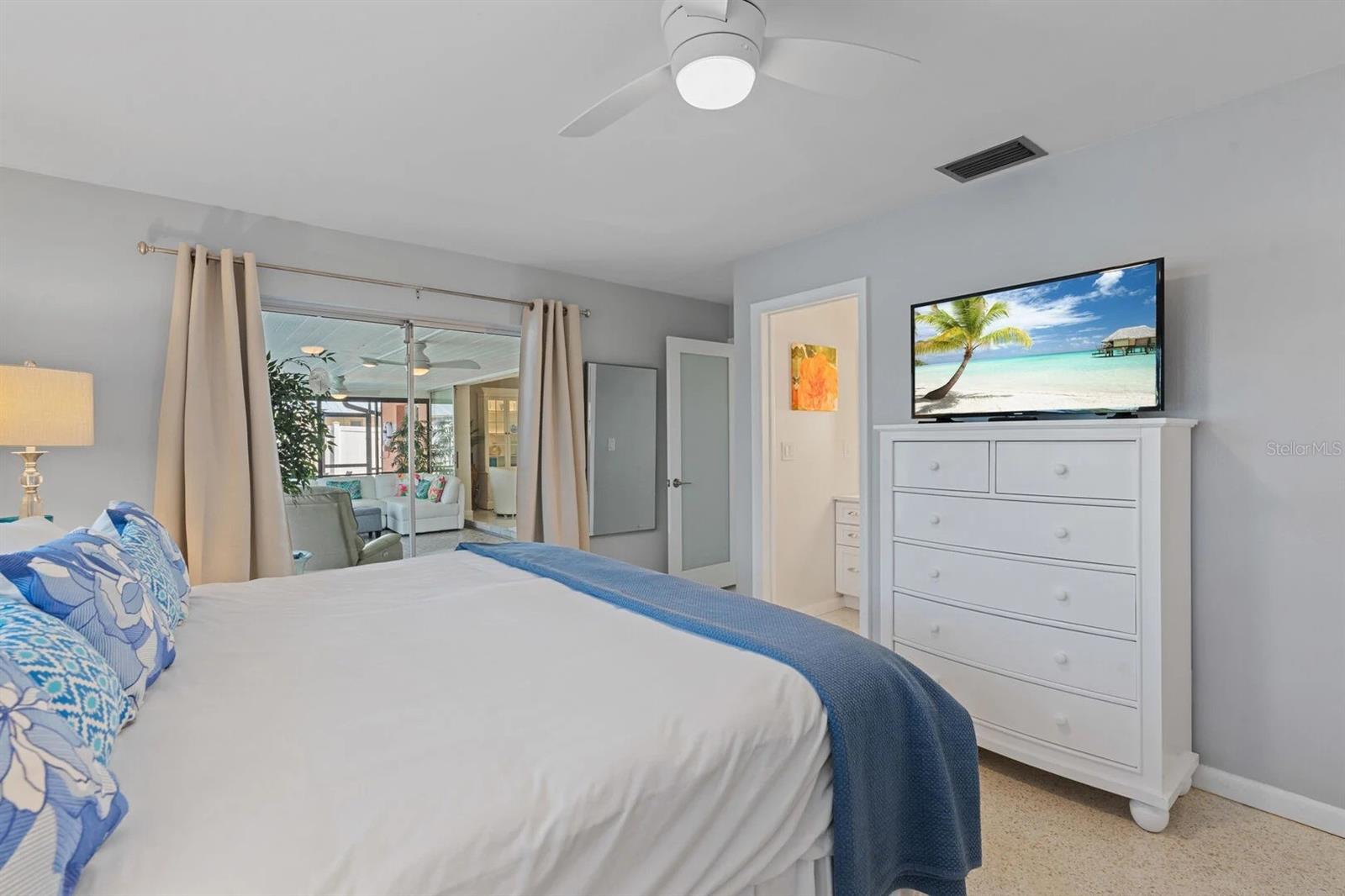 Furnished bedroom with blue-and-white bedding, a white dresser, and sliding glass doors to the living area.