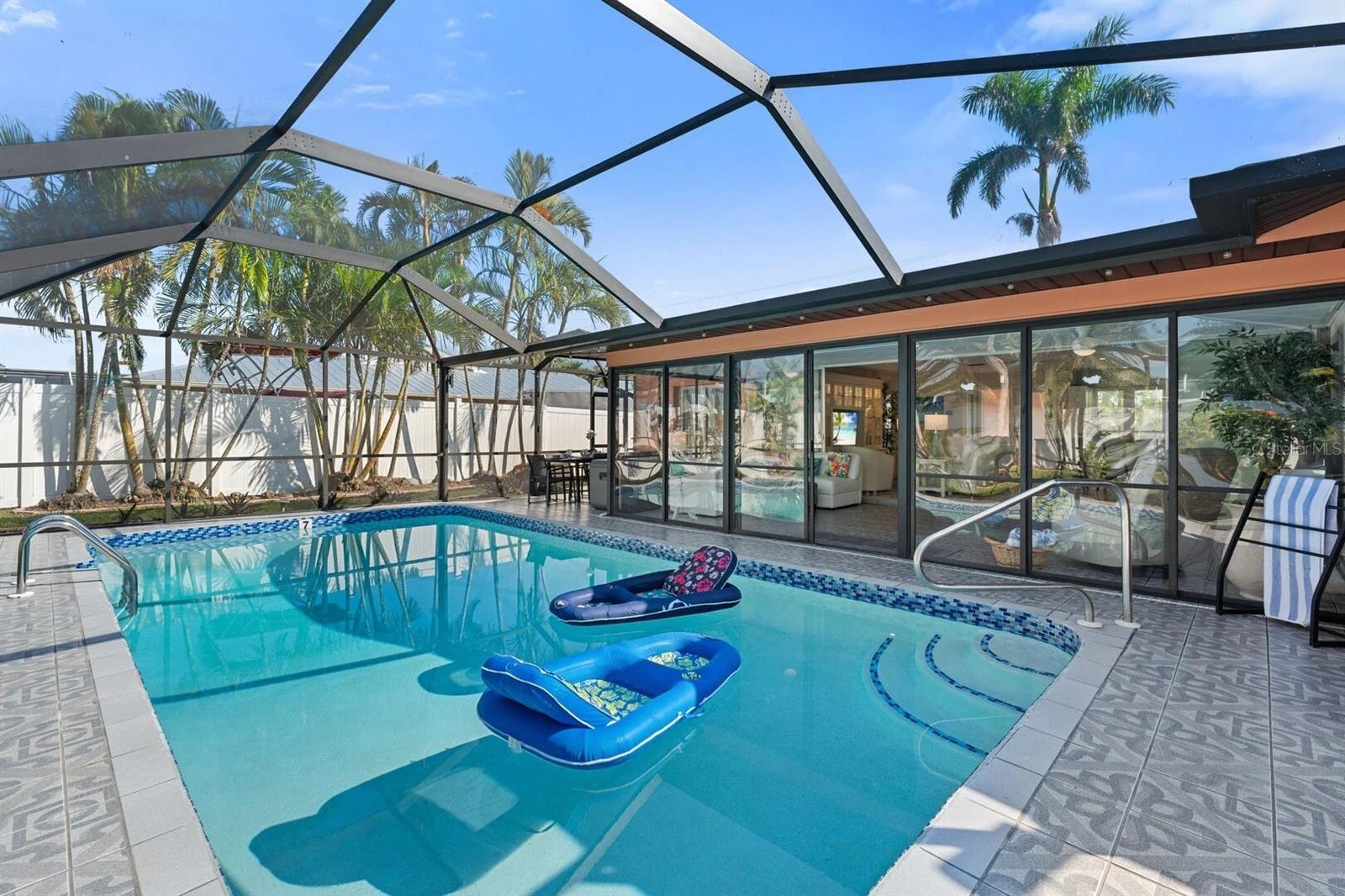 Screened pool with blue floats beside sliding glass doors and a palm-lined patio.