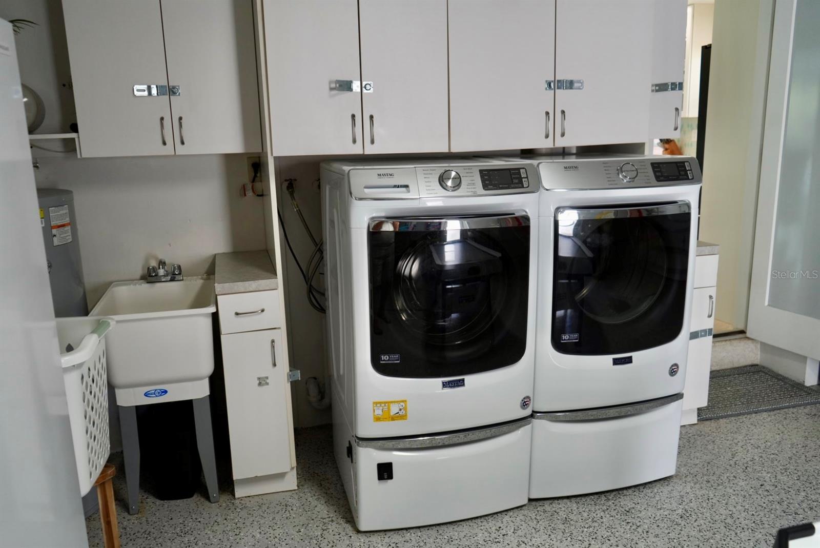 Laundry room with two Maytag front-loading machines, overhead cabinets, and a utility sink.