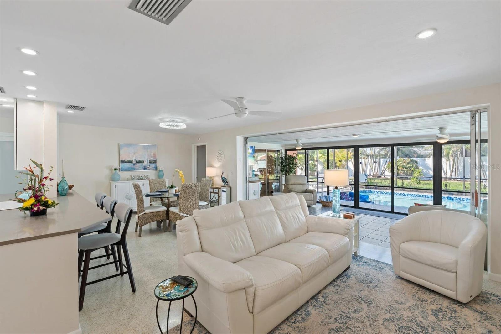 Open-plan living room with white leather seating and sliding doors overlooking the pool.