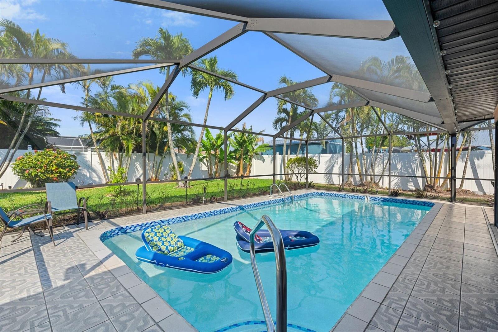 Backyard pool beneath a screened lanai, with inflatable loungers and tropical palms.