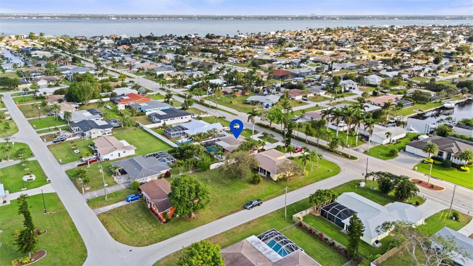 Aerial neighborhood view with a blue pin marking a home near canals and a broad expanse of water.