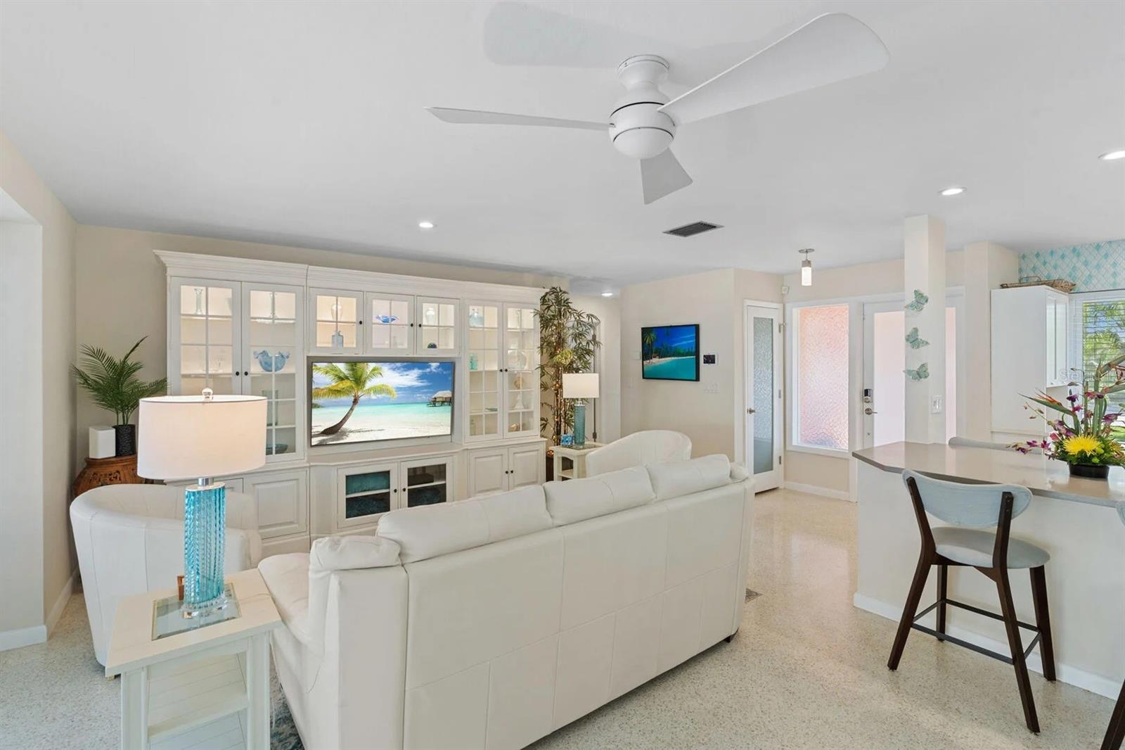 Living room with a white sectional, built-in display cabinets, ceiling fan, and adjoining breakfast counter.