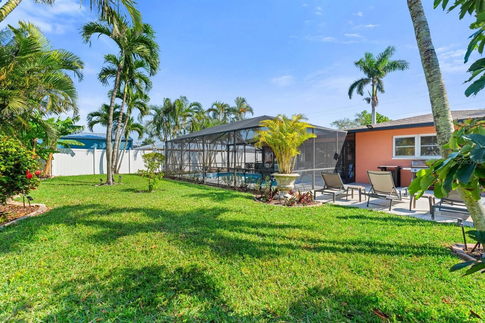 Tropical backyard with a screened-in pool, patio lounge chairs, palm trees, and a broad green lawn.