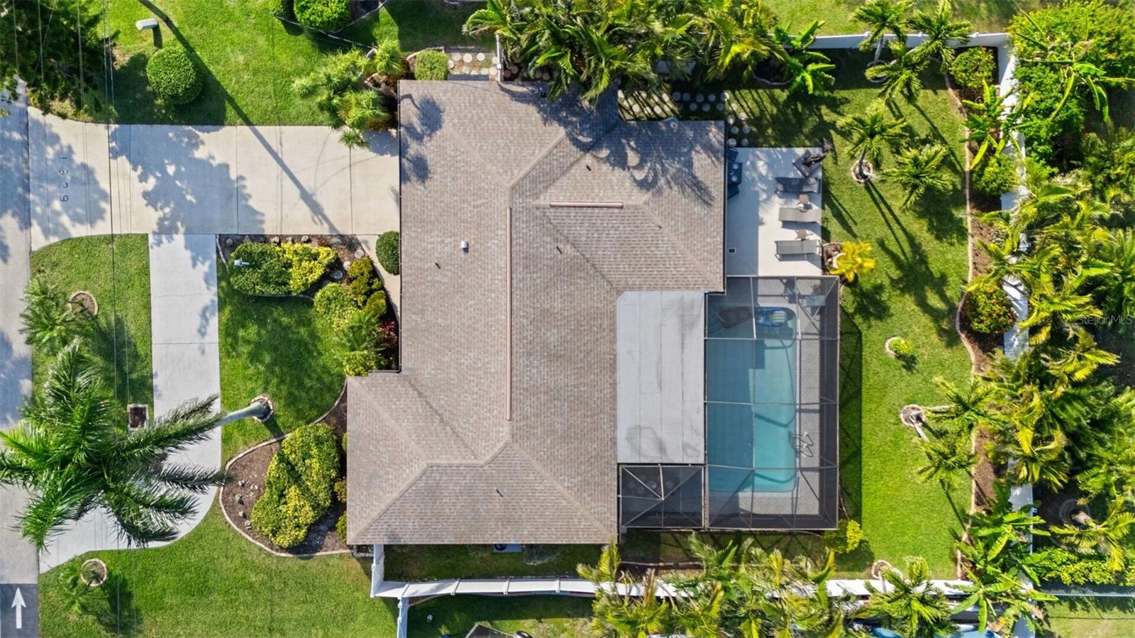 Aerial view of a home with a screened pool, patio, and palm-lined landscaped yard.