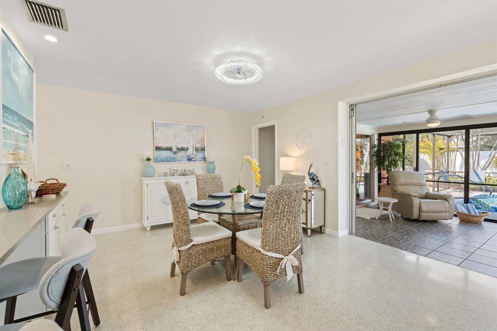 Dining room with woven chairs and a glass table opening to a lanai overlooking the pool.