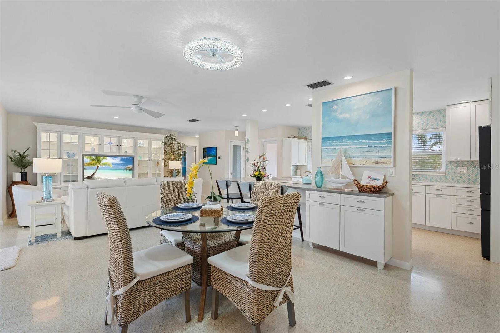 Open-plan dining and living area with woven chairs, white built-ins, and an adjoining kitchen.