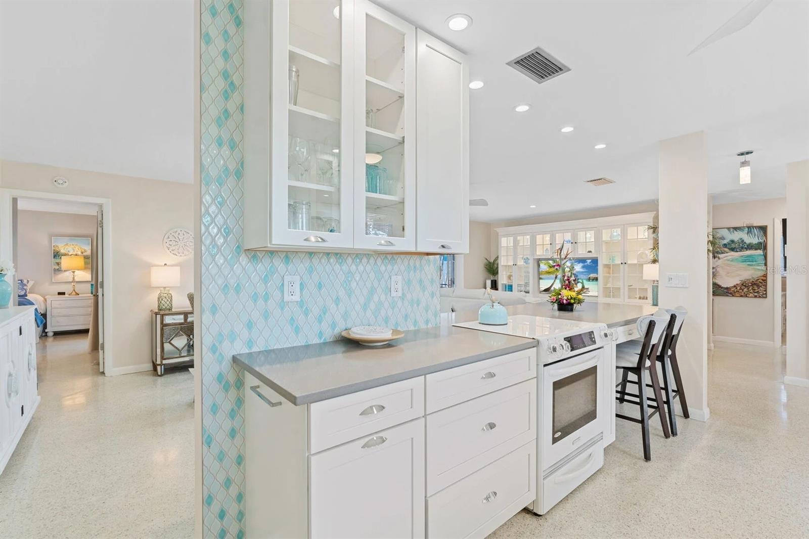 Open kitchen with white cabinetry, a large island, and turquoise patterned tile backsplash.
