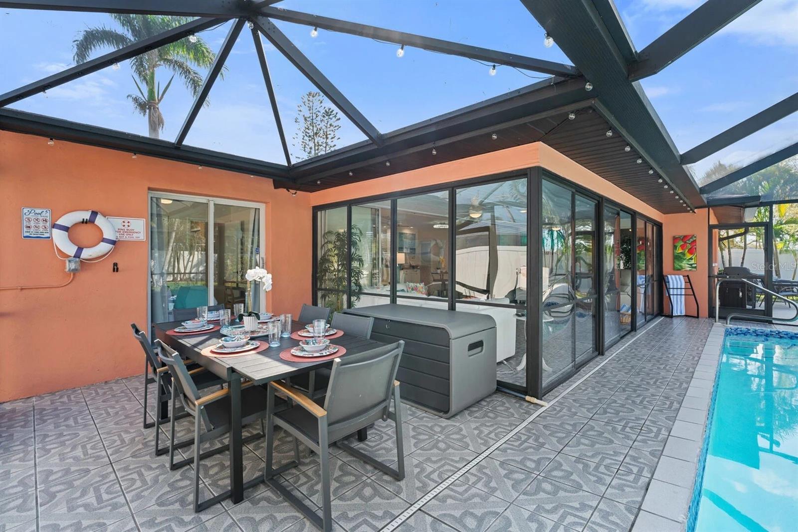 Screened lanai with a tiled pool deck, outdoor dining set, and sliding glass doors.