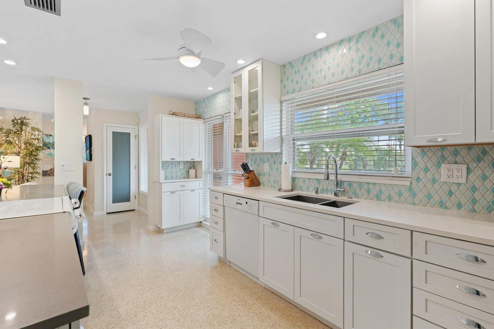 Bright kitchen with white cabinets, turquoise patterned backsplash, and a sink beneath wide windows.