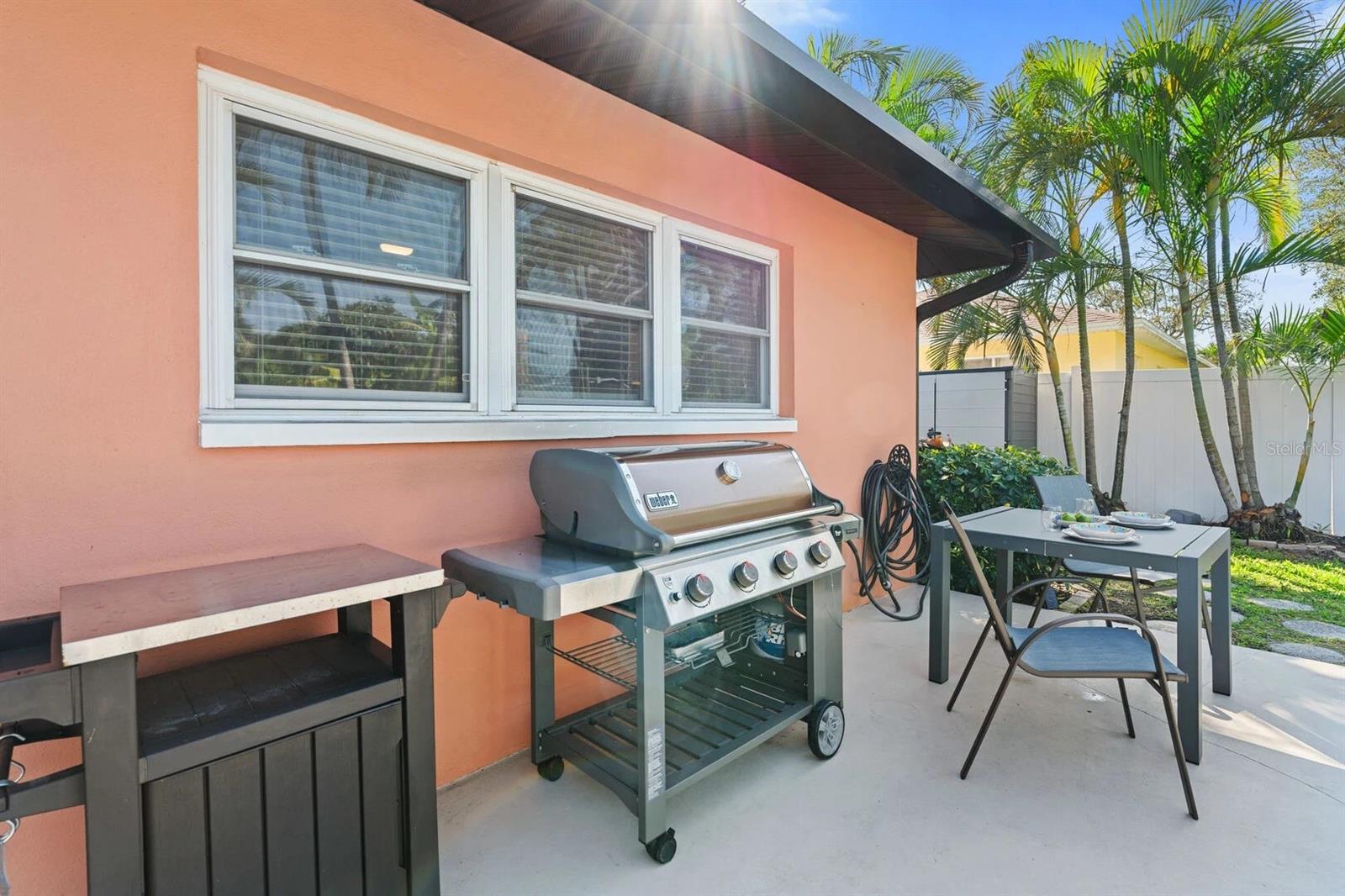 Patio with a gas grill, outdoor dining set, peach stucco wall, and palms.