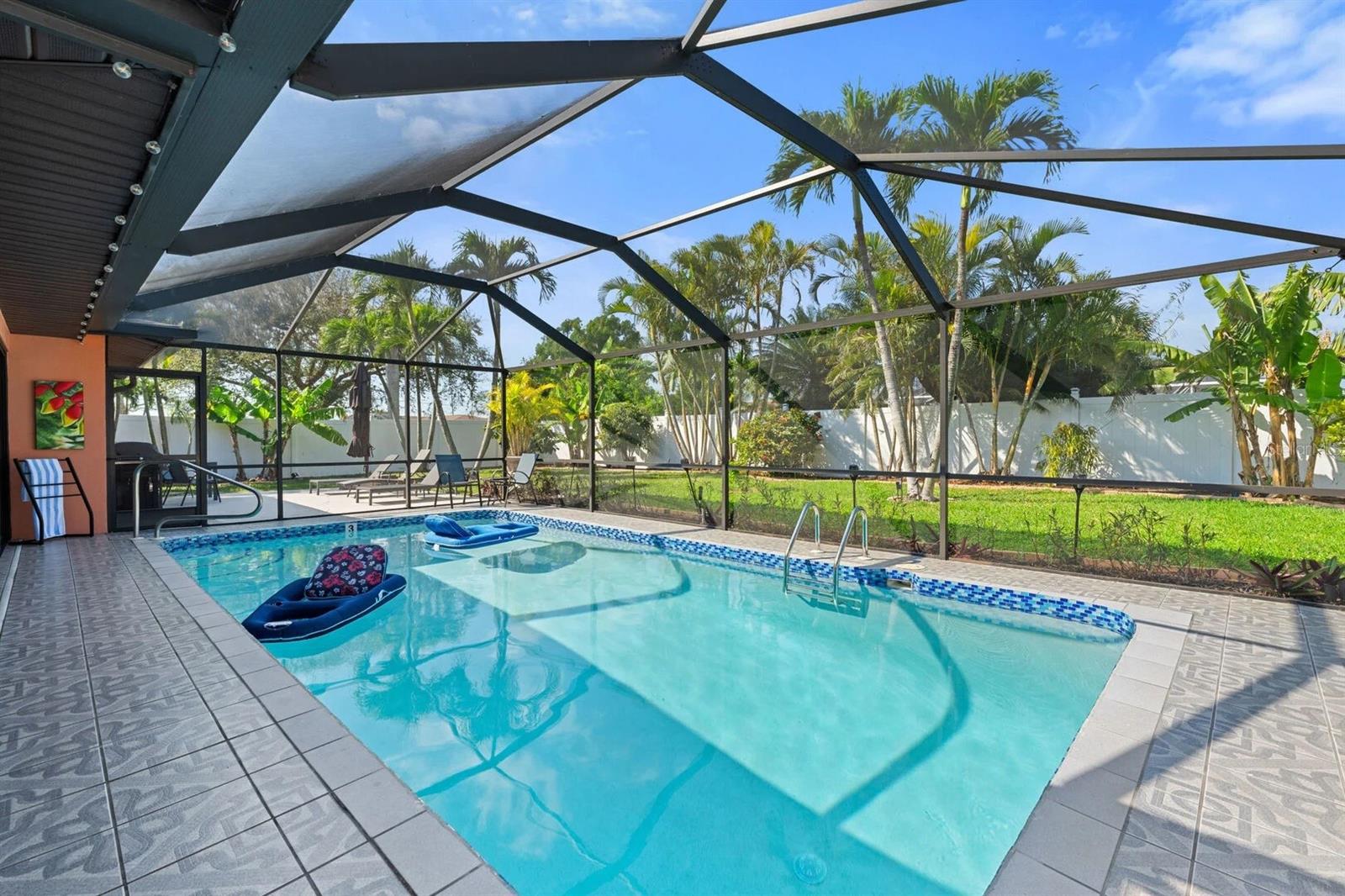 Swimming pool beneath a screened lanai, with lounge chairs and tropical palms.