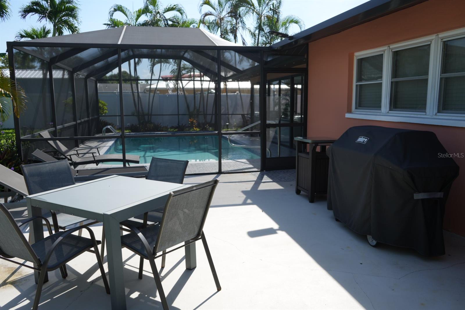 Screened pool and furnished patio with an outdoor dining table and covered grill.