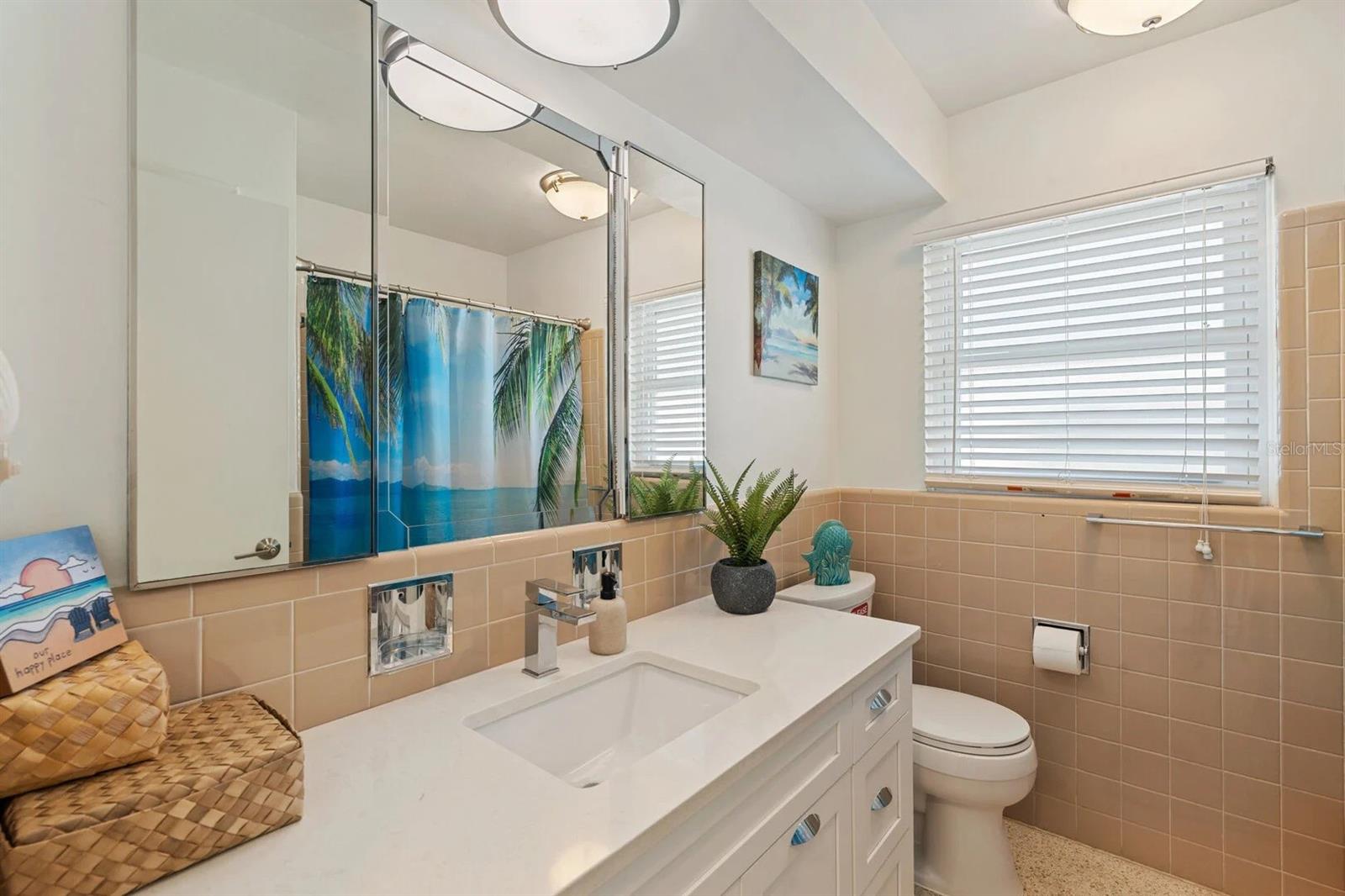 Bathroom with white vanity and mirrored cabinet, peach tile, and a window with blinds.