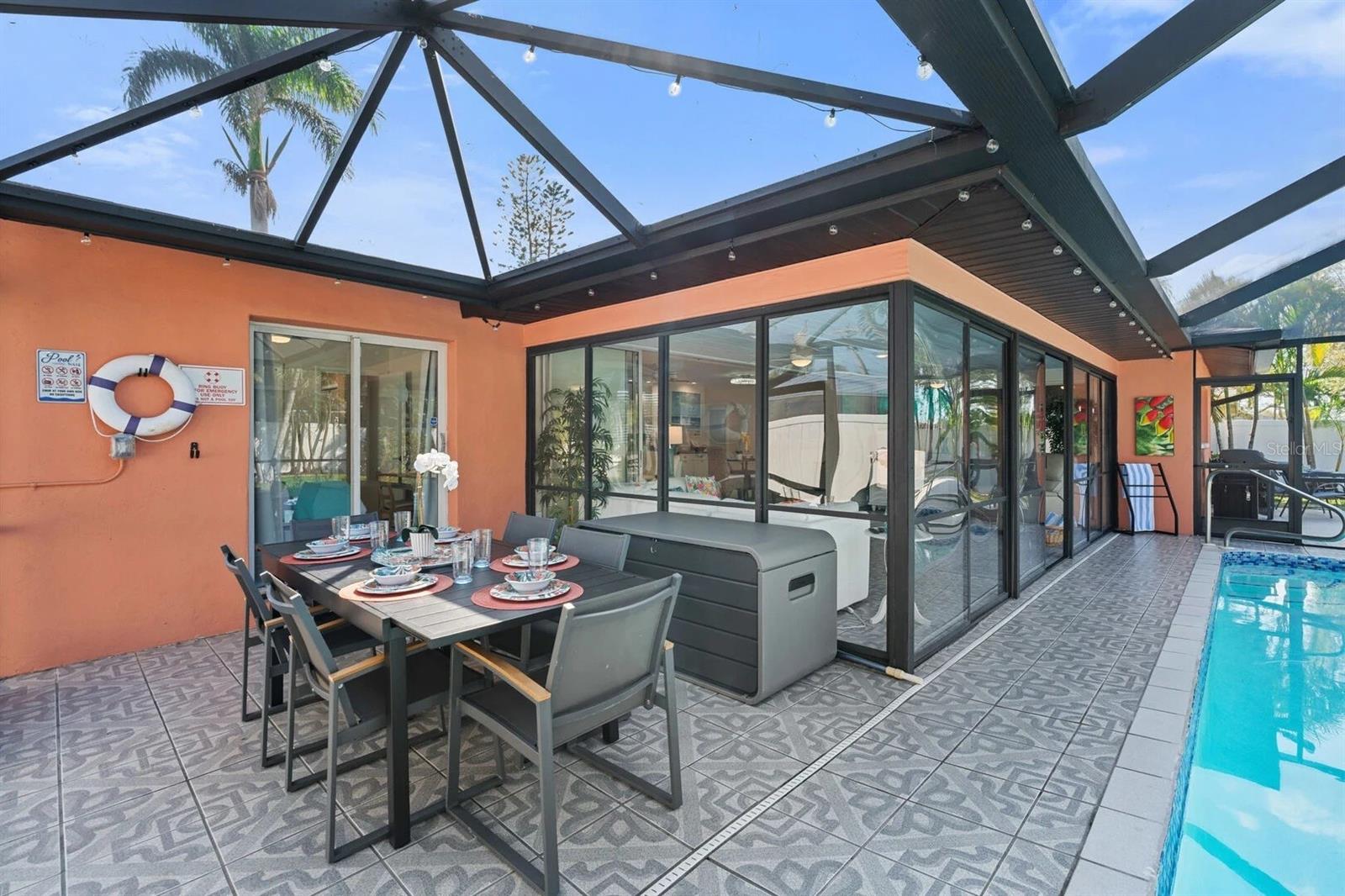 Screened lanai with an outdoor dining table beside a swimming pool and sliding glass doors.