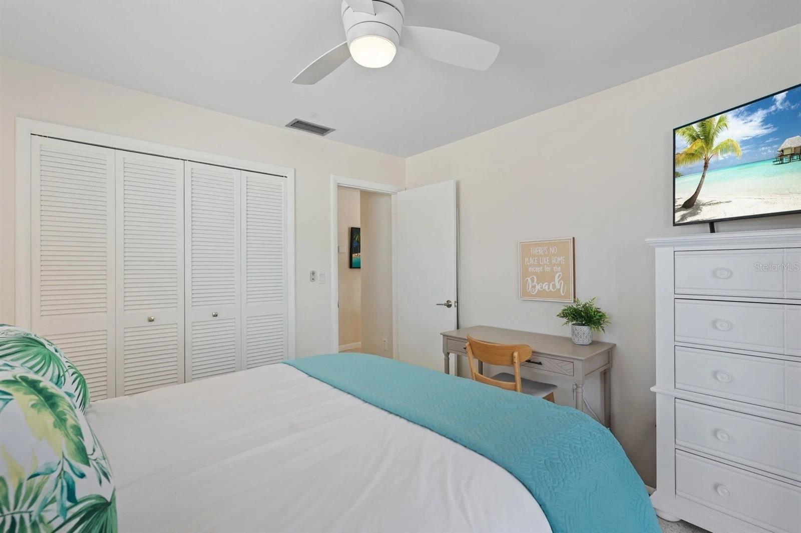 Bedroom with a turquoise bed runner, louvered closet doors, a small desk, and beach-themed decor.