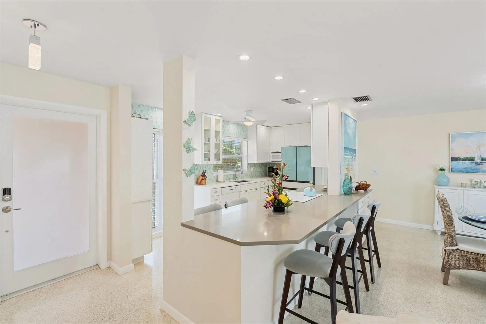 Open kitchen with white cabinets, a large bar peninsula, and light terrazzo flooring.