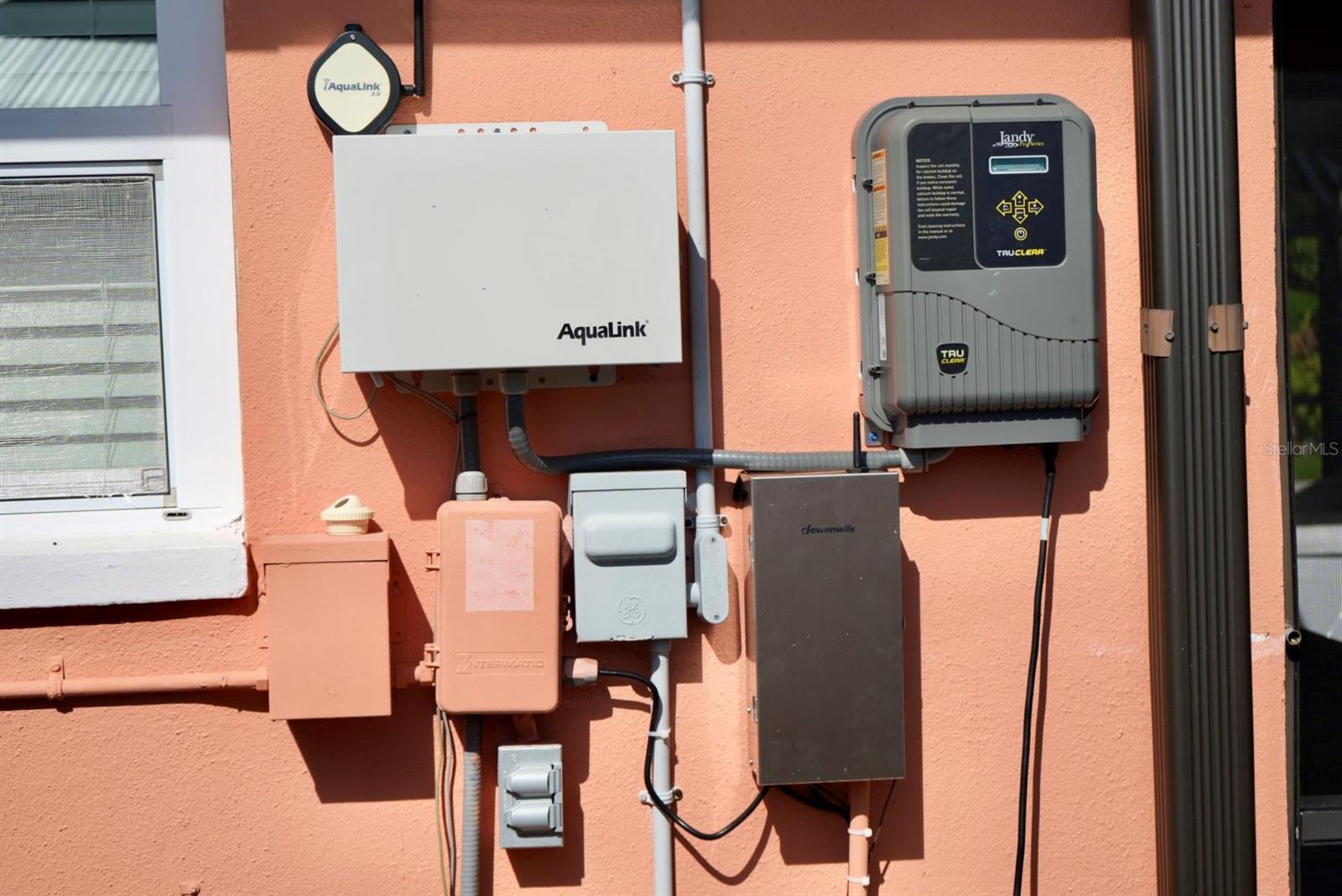 Pool control equipment mounted on a coral exterior wall, including AquaLink and Jandy TruClear systems.