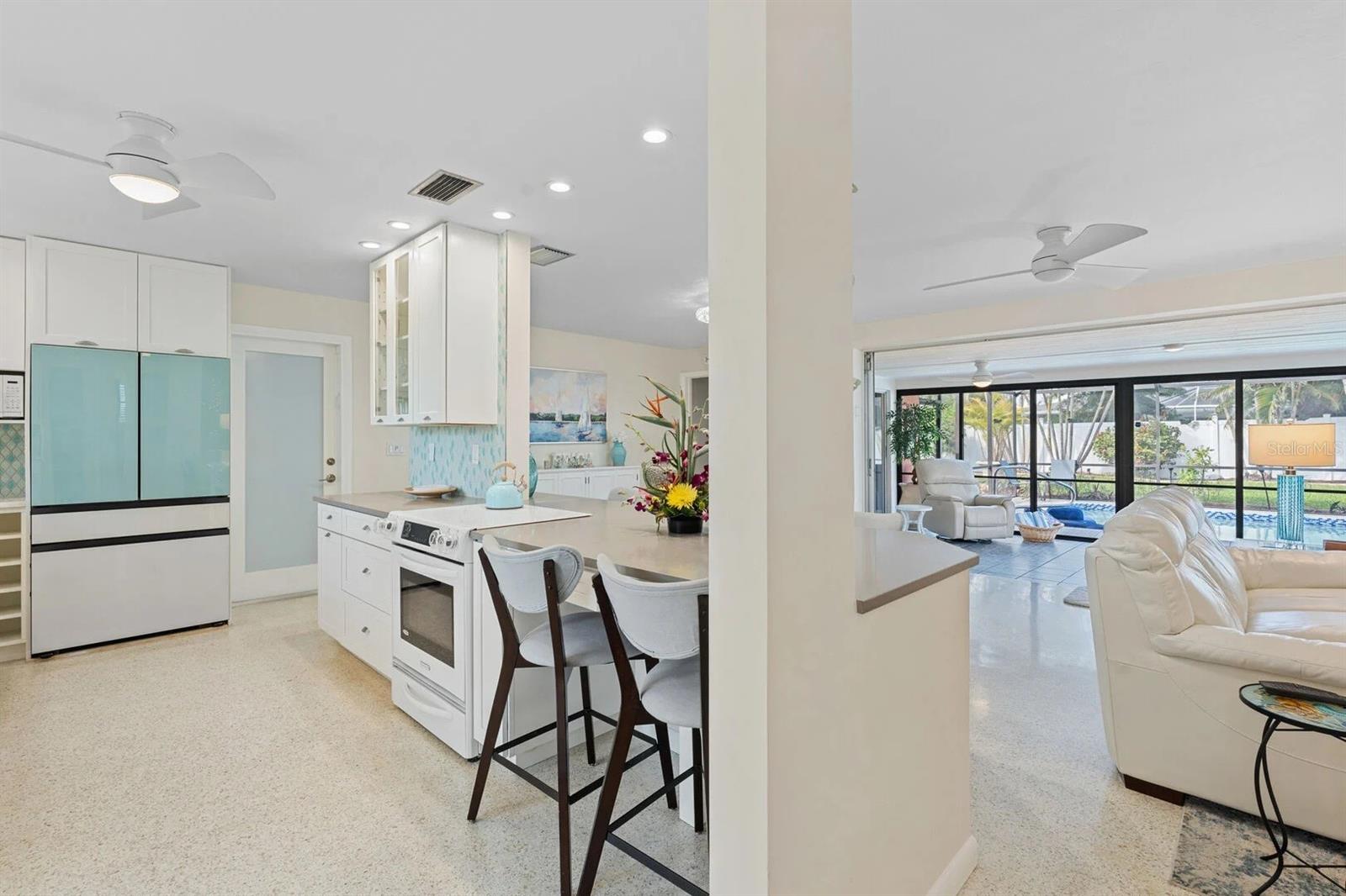 Open kitchen and living room with white cabinetry and views through glass doors to the pool.