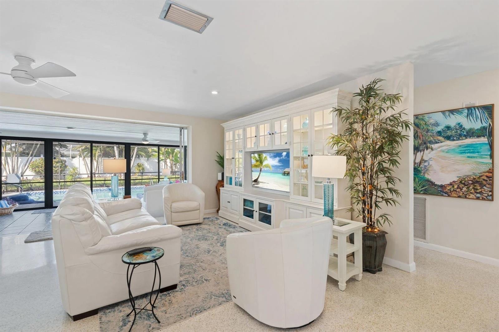 Furnished living room with white sofas, built-in cabinets, and sliding doors overlooking a screened pool.