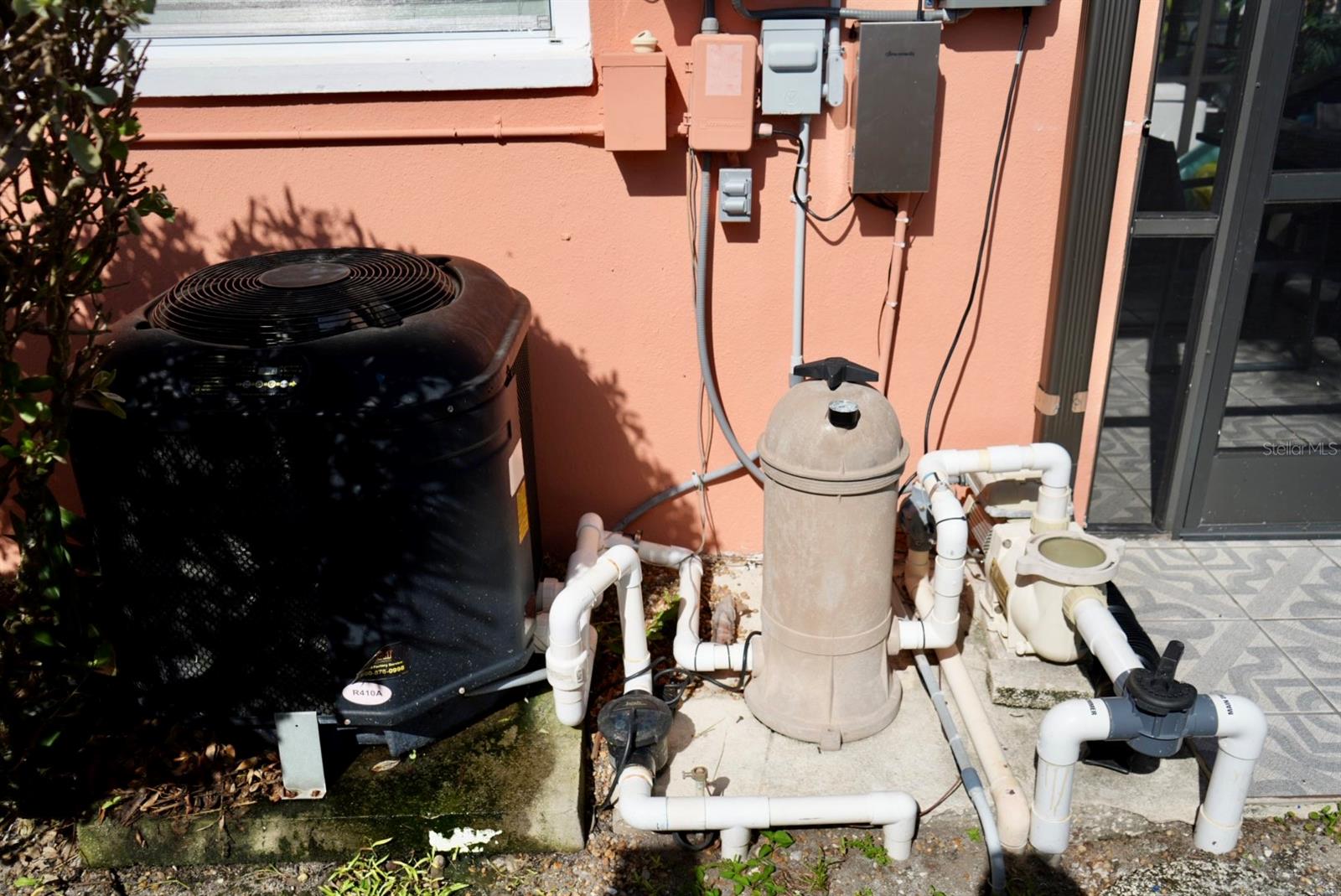 Air-conditioning condenser and pool filtration equipment beside the home’s peach-colored exterior wall.